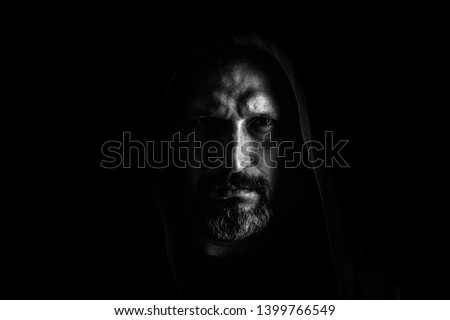 Brutal man with a gray beard in the hood with sharp shadows on a black background. Copy space.