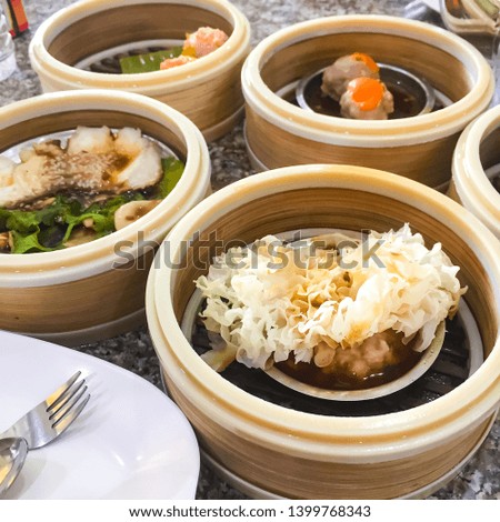 Dim sum , this is a popular Chinese food which were steamed. They are in the small bamboo basket. In the picture, there are many baskets in the wooden table which has food, pork wrapped in seaweed , s
