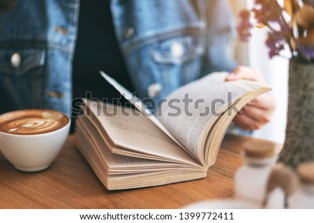Closeup image of a woman holding and reading a vintage novel book while drinking coffee Royalty-Free Stock Photo #1399772411