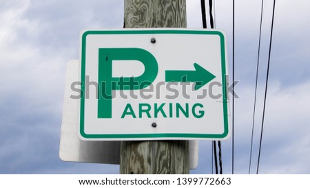 Directional signpost for parking area, against a cloudy sky.