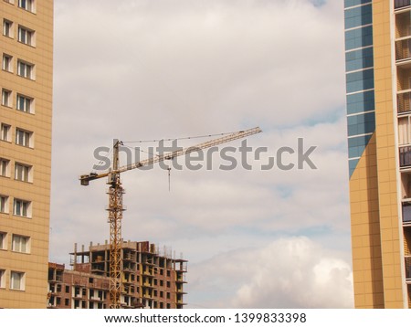 Construction of a high-rise building. High-altitude crane. The frame between the two walls. Background sky with clouds.                               