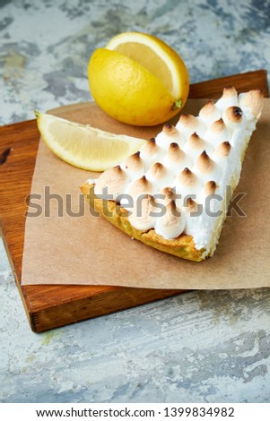 A piece of lemon tart decorated with a slice of lemon on a wooden board. Gray textured background. Beautiful serving dishes. Dessert. Food chain