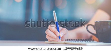 Woman hand is writing on a notepad with a pen in office.Web banner.