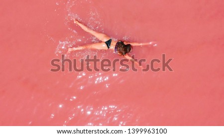 Aerial view of an attractive woman in a bikini floating in pink salt lake.