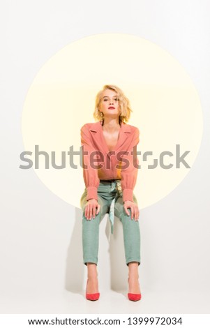 beautiful stylish girl looking at camera and posing while sitting on yellow circle with white background