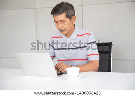 Senior Asia businessman in casual  work by use laptop in his office and have coffee near him