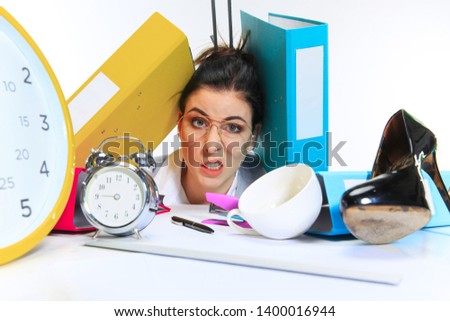 Seriously. Young woman getting a lot of work and deadline, being under the pressure of the deals. Pressed by folders with papers. Concept of office worker's troubles, business, problems and stress.