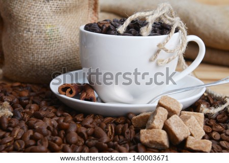 Roasted coffee beans with cup on jute hessian background