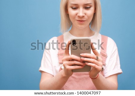 Smartphone in the hands of a teen girl. Close-up photo of a blond girl in cute clothes uses a smartphone on a blue background, the focus on the phone in the hands of the girl. Copyspace