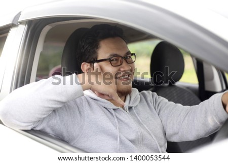 Portrait of young Asian male driver smiling and make call me sign gesture in his car