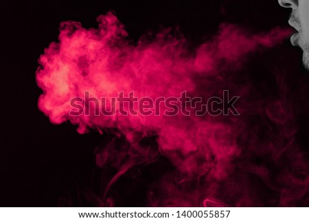 Portrait of a side mouth part of guys face with a colored backlight of monochrome smoking a vape and exhaling pink in different directions on a black isolated background. Puffs harmful to health.