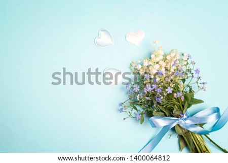 A bouquet of lily of the valley and forget-me-nots with a ribbon on a blue background. Copy space, top view.