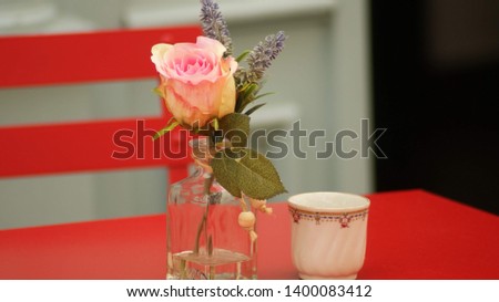 pink rose in a glass of water next to a cup of coffee on a red table