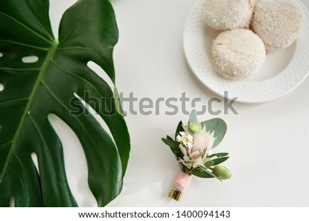 Top view of wedding boutonniere, fresh green monstera leaf and french macaroons on white wood table background, copy space. Wedding details. Flat lay, overhead shot, above