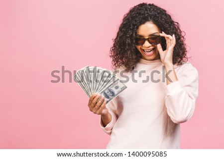 Cool rich girl! Money winner! Surprised beautiful african american woman in casual holding money in sunglasses isolated against pink background.