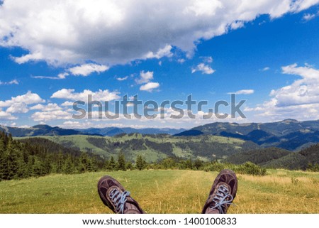 landscape consisting of a Carpathians mountains with legs sticking out and green grassy valley in the foreground  and cloudy sky on the background