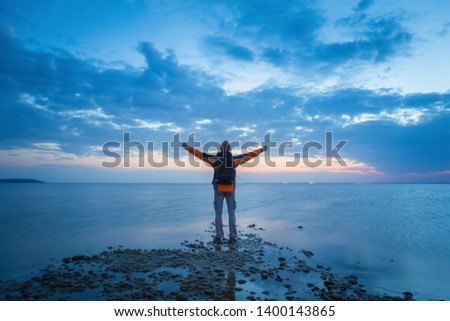 Young man staying on the edge of a sea shore and enjoying the sunset.