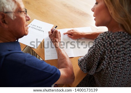 Woman Helping Senior Man To Complete Last Will And Testament At Home Royalty-Free Stock Photo #1400173139