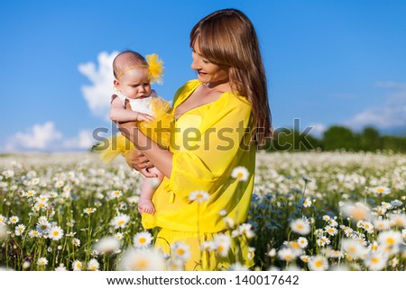 Beautiful young mother playing with her ??daughter in field of daisies