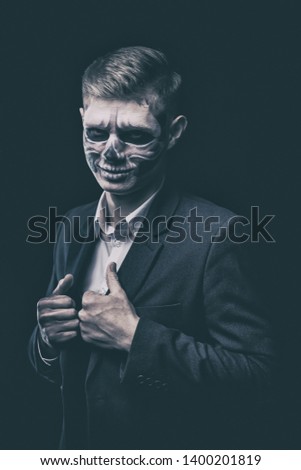 Stylish and beautiful, emotional young man with skeleton makeup in a strict suit against the background of smoke and dark background to Halloween