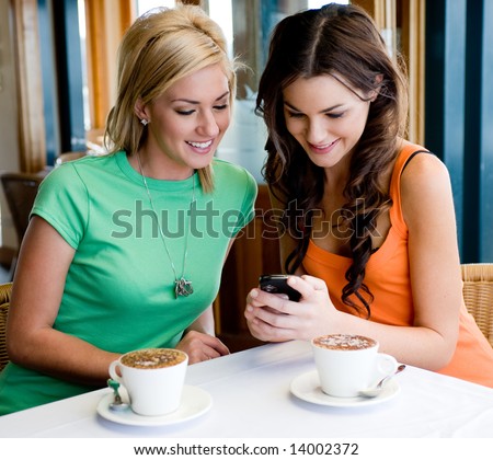 Two young attractive women drinking coffee at a restaurant and looking at phone Royalty-Free Stock Photo #14002372