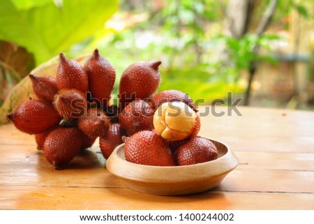Whole and peeled of Salacca(Salacca wallichiana) in bowl and its bunch on table with blurred garden background.Have a lot of fiber,vitamins and minerals.Food,Fruits or healthcare concept.