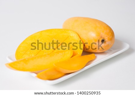 Yellow mango and slices of mango are on the white plate.  Isolated background