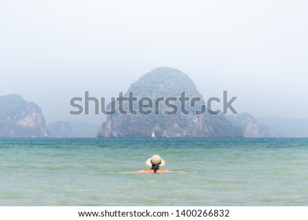 Woman in straw hat swiming in the sea in Krabi Railey beach overlooking the harbour and mountains, Thailand.