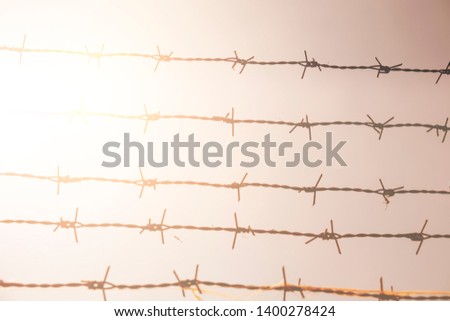 High fence with barbed wire in sunset