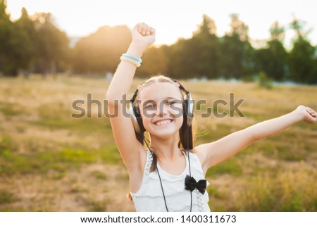 happy girl having fun on nature, active child with black and silver headphones listening music and dancing Royalty-Free Stock Photo #1400311673