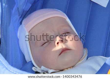 Face of a newborn baby sleeping in a stroller. Sleeping baby lying in the stroller. Peaceful infant girl while Hiking in winter. Picture of a newborn in the pink hat and blue overalls.