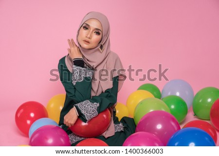 
Beautiful girl with colorful air balloons laughing over pink background. Happy Muslim girl on birthday holiday party. Joyful model having fun, playing and celebrating with multi color balloon.