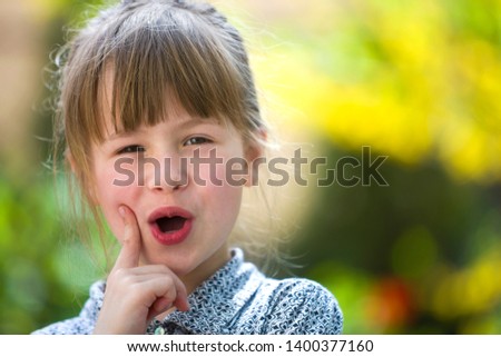 Cute pretty child girl with funny expression outdoors on blurred sunny green and yellow bright background.