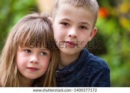 Two cute fair-haired children siblings, young boy brother and sister girl outdoors on bright sunny green bokeh background. Family relation, friendship and love concept.
