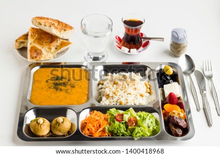 Ramadan iftar meal in the stainless steel,portion food tray on the white surface with;tea,water and Ramadan bread