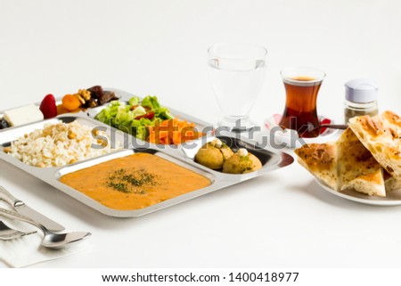Ramadan iftar meal in the stainless steel,portion food tray on the white surface with;tea,water and Ramadan bread.