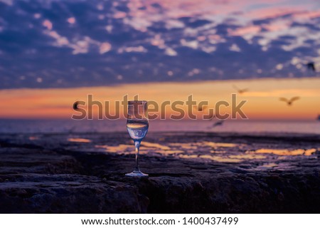 Romantic glass of wine sitting on the beach at colorful sunset Glasses of white wine against sunset, white wine on the sky background with clouds