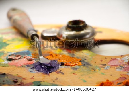 Closeup of palette with colorful paints and spatula on white surface, background or concept