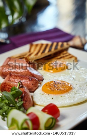 Breakfast course closeup macro picture - fried eggs, sausages and vegetables. Blurry colorful background
