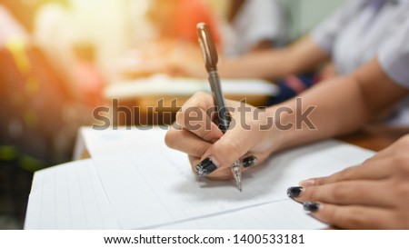 Student writing or taking test in  classroom for midterm or final examination; education concept closed up picture of learner holding a pen taking lecture note in a study room of college or university