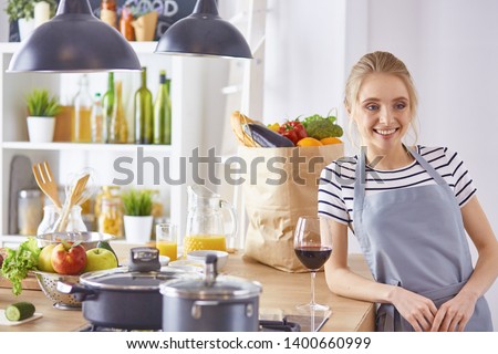 Beautiful woman in kitchen is drinking red wine