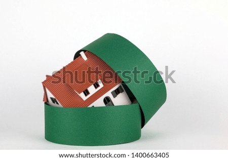 Model of two-storey house and green round gift box on the white background. House painted white under a tiled roof.