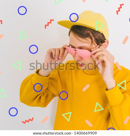 portrait of handsome boy in pink painted sunglasses, yellow baseball cap and oversize pullover among memphis geometry figures. crazy surreal art  