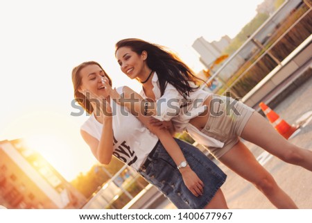 Two beautiful carefree girlfriends have fun in the parking on the background of evening sunset city, summer time, horizon line crooked