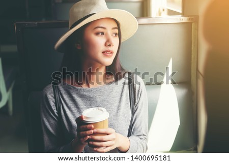 Beautiful Asian women wearing hat holding a cup of hot coffee sitting in train.