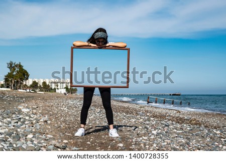 Young girl is holding empty frame and going through it. Double exposure