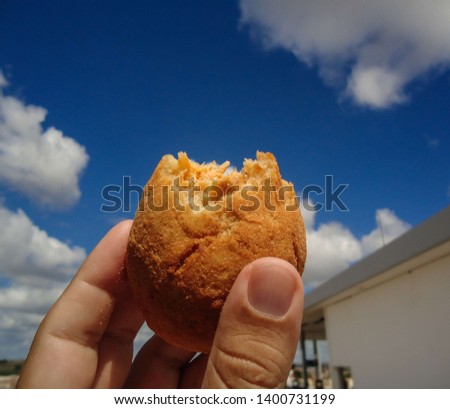 Holding a COXINHA DE FRANGO and having blue sky with cloud as background. The COXINHA DE FRANGO is a very popular food in Brazil. This image was produced in May 2019. Royalty-Free Stock Photo #1400731199