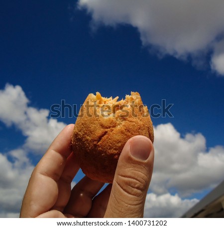 Holding a COXINHA DE FRANGO and having blue sky with cloud as background. The COXINHA DE FRANGO is a very popular food in Brazil. This image was produced in May 2019. Royalty-Free Stock Photo #1400731202