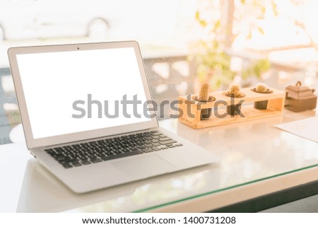 Laptop with white blank screen to insert picture or text on table at cafe with cactus and orange sunlight in the moring