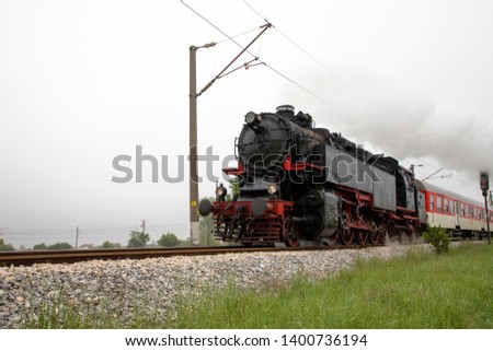 Vintage steam engine locomotive speeding on railroad tracks curve and blowing heavy white smoke.